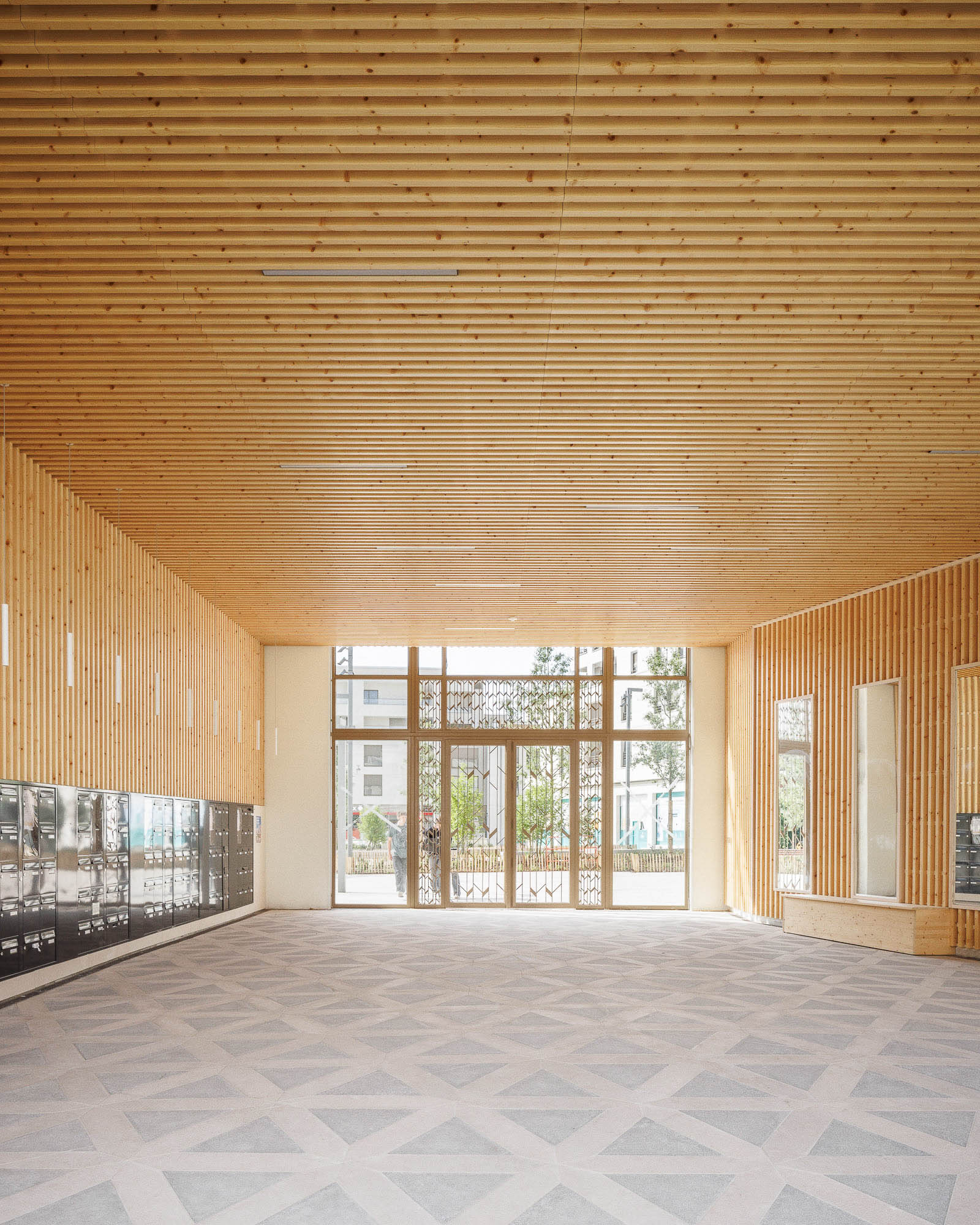 Vue sur la rue depuis le hall intérieur / extérieur sous porche en bardage bois d'un immeuble ZAC Jean Zay à Antony par Cussac Architectes et Associés (ca+a), où pénètre la lumière naturelle.